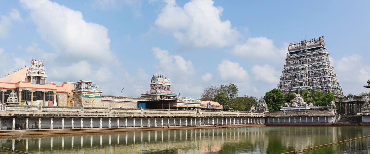 A temple complex with a large, multi-tiered tower and a calm river in the foreground.