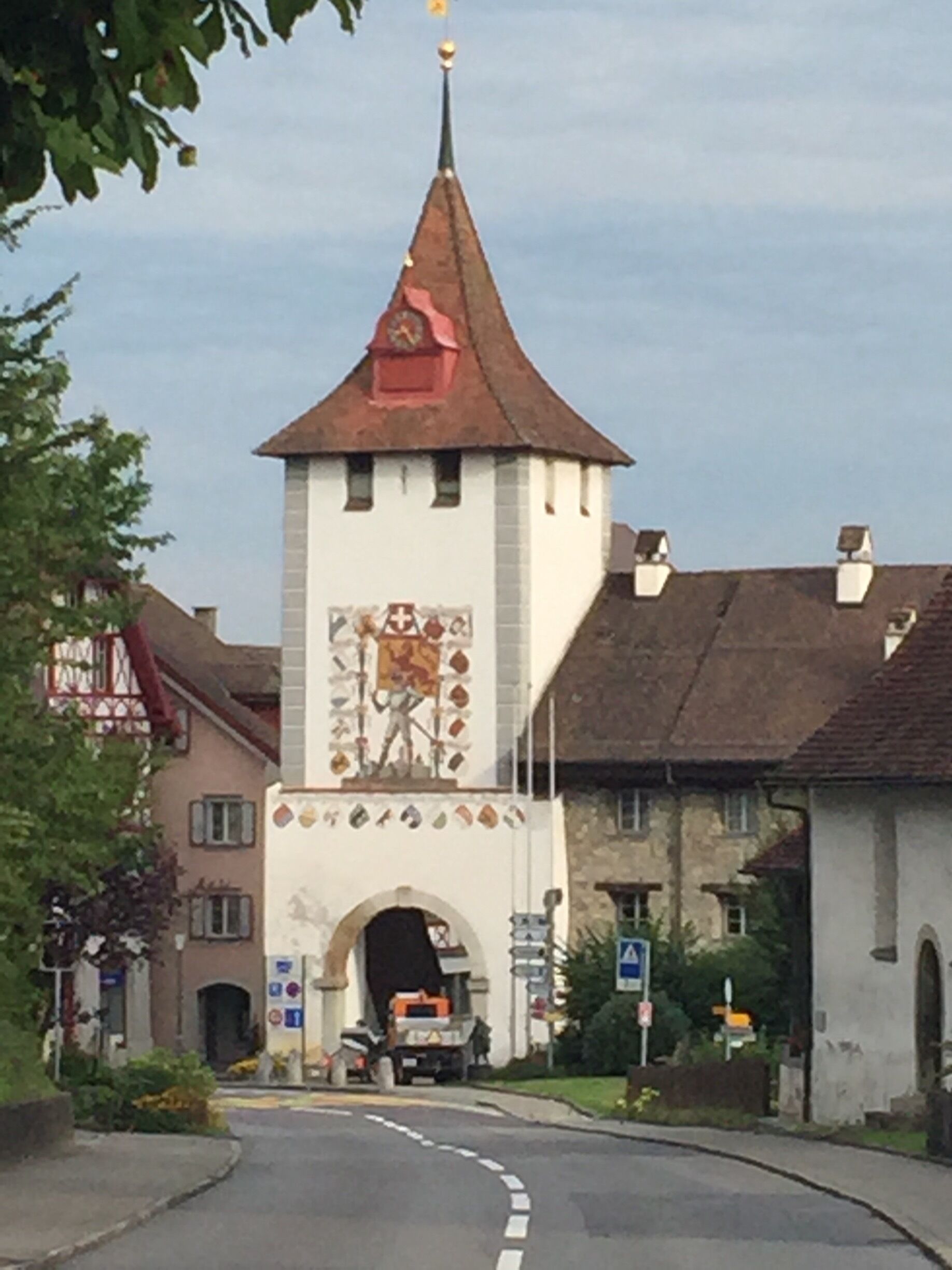 A tower with a clock and a mural, surrounded by buildings and a road.