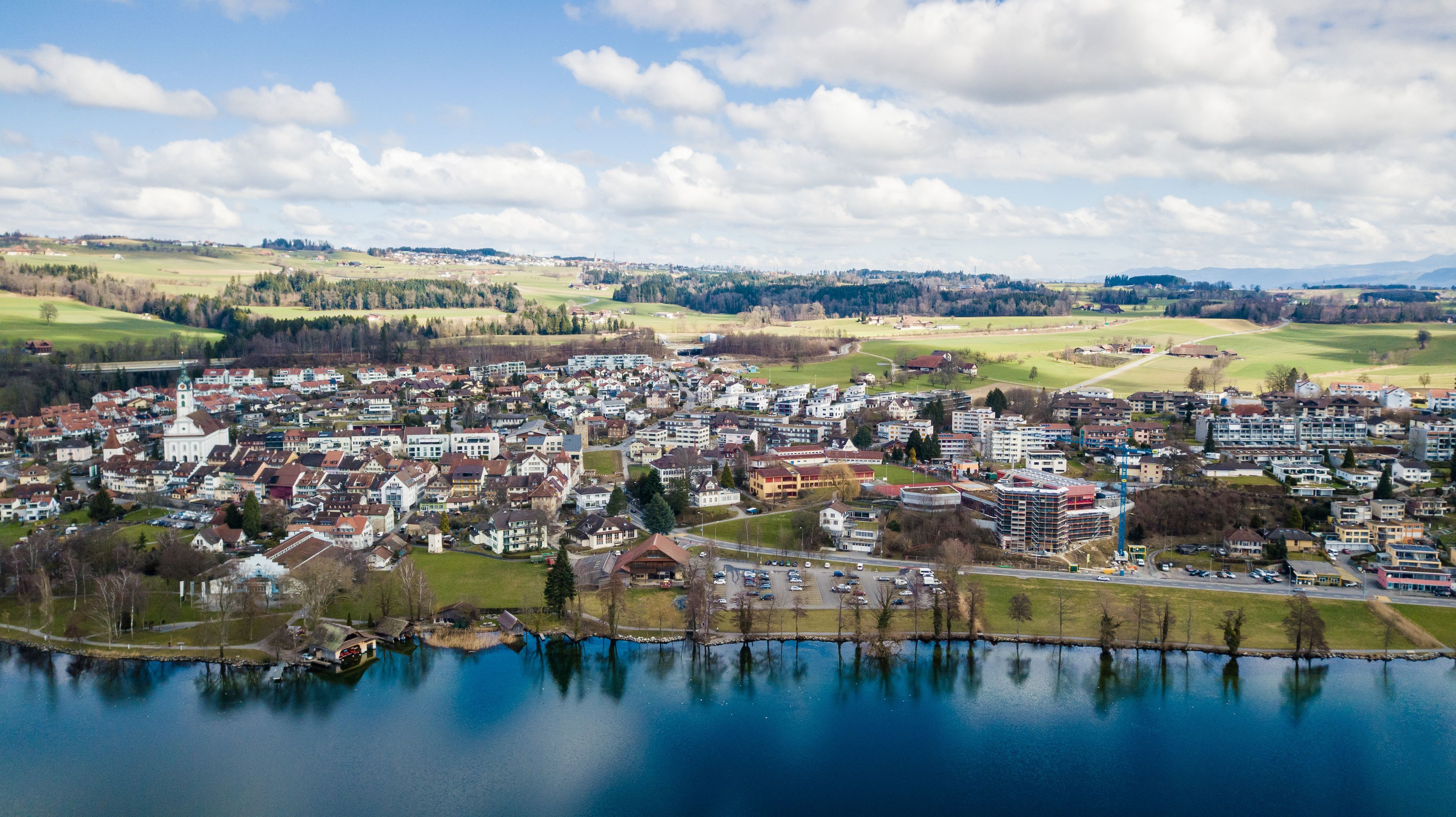 A lakeside town with buildings, a church, and surrounding fields.