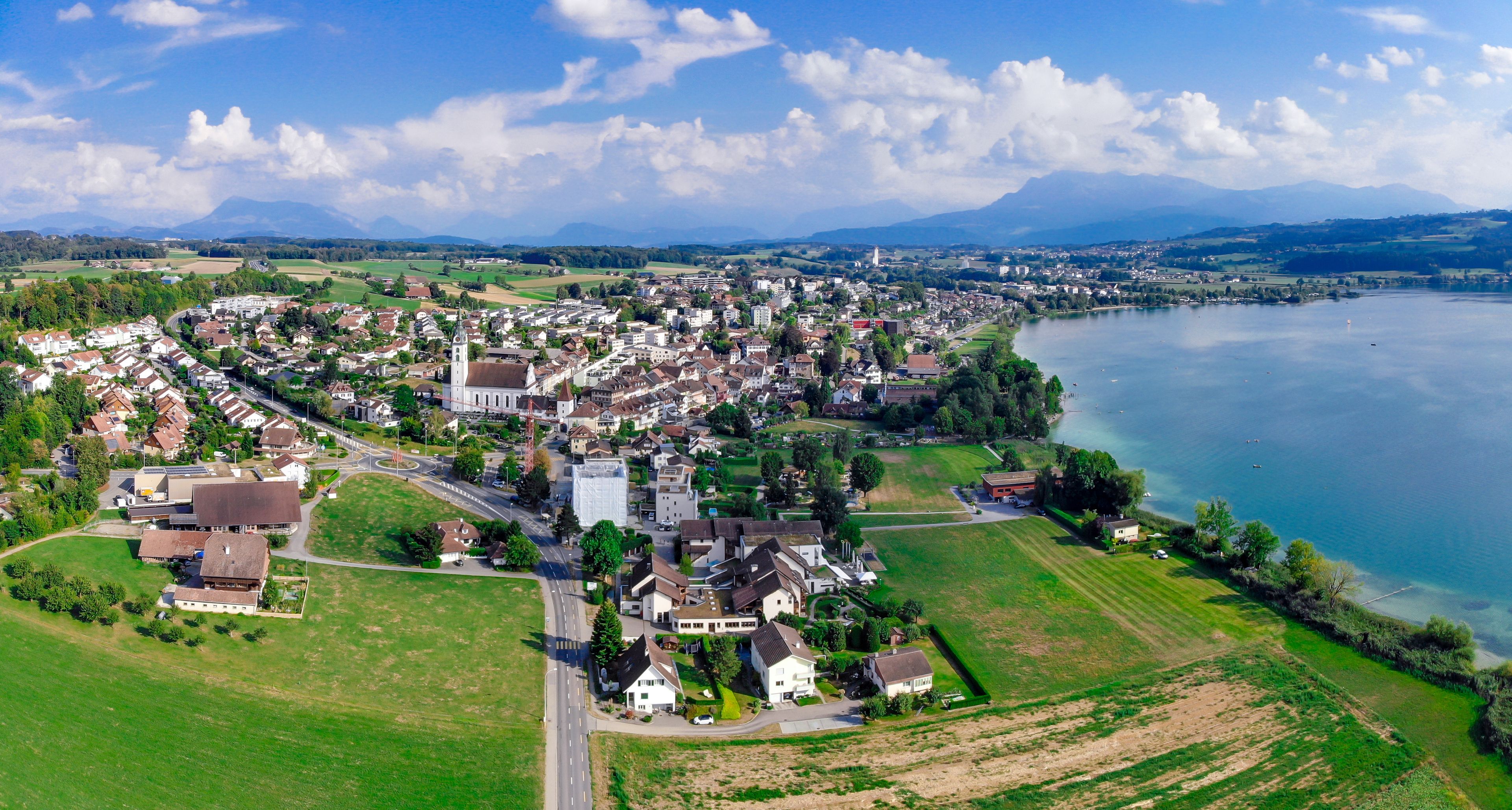 An aerial view of a town by a lake with a prominent church, surrounded by green fields and residential areas.