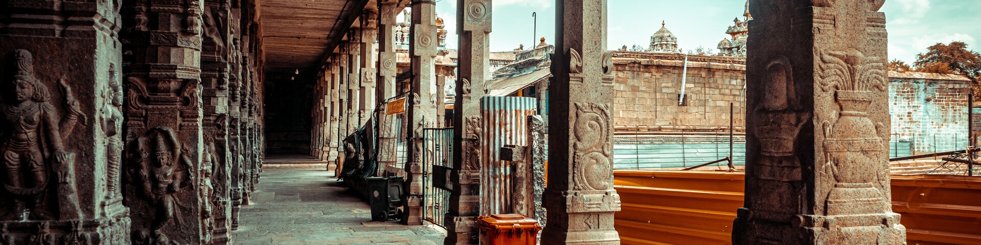Un pasillo con esculturas de piedra y columnas, que conduce a un templo con barandilla dorada.