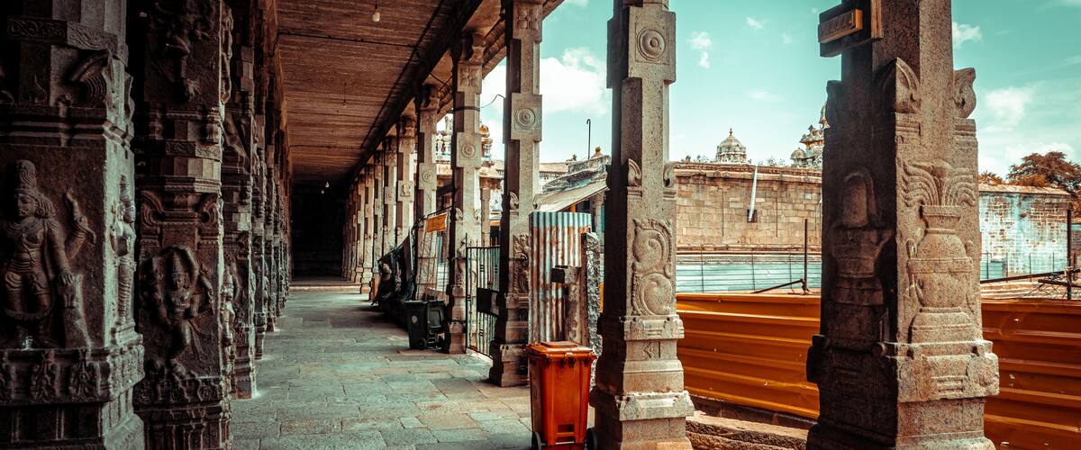 A corridor with stone carvings and columns, leading to a temple with a golden railing.