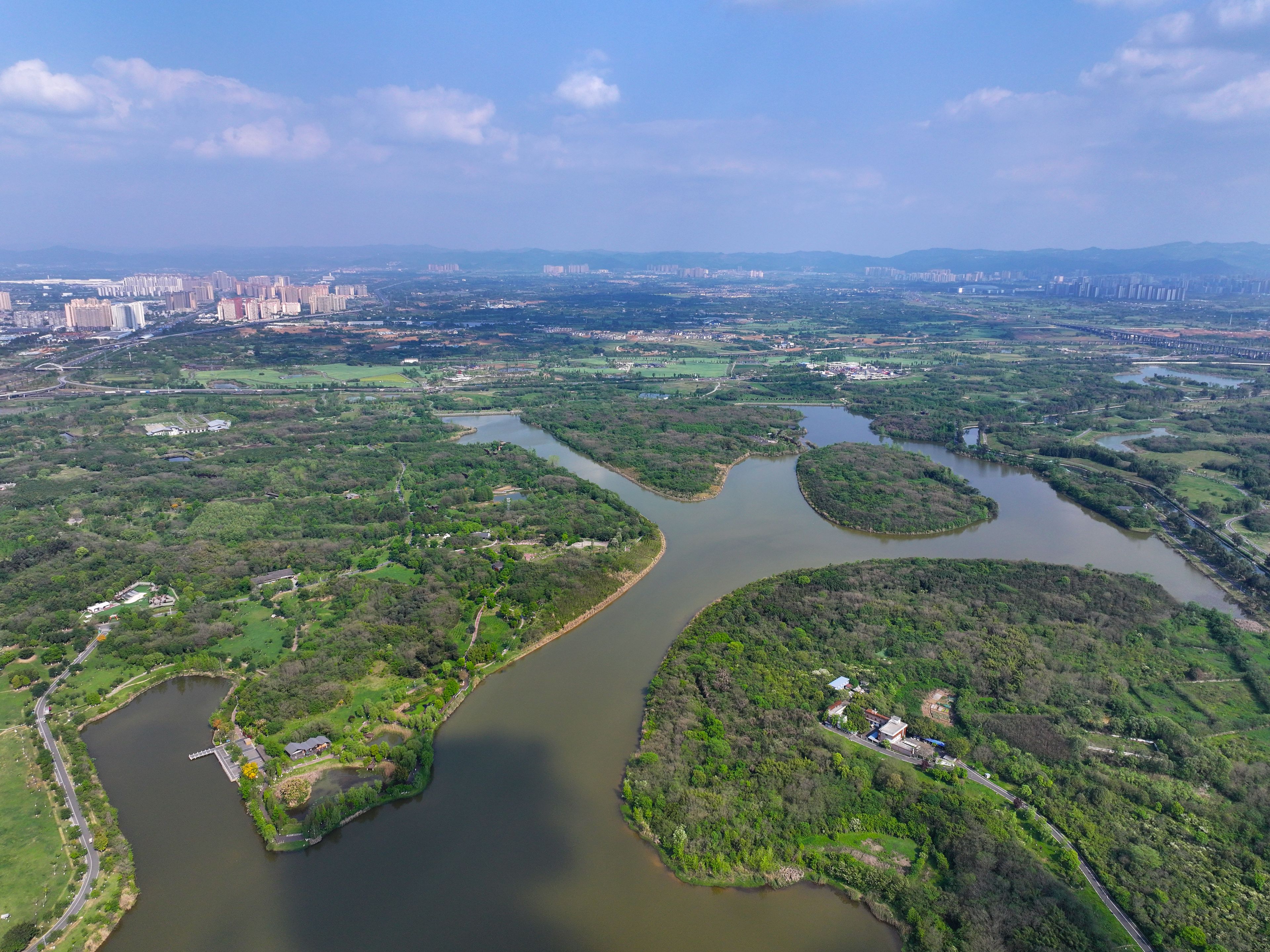 Luchtbeeld van een rivierdelta met diverse waterlopen, omringd door weelderige begroeiing en stedelijke bebouwing op de achtergrond.