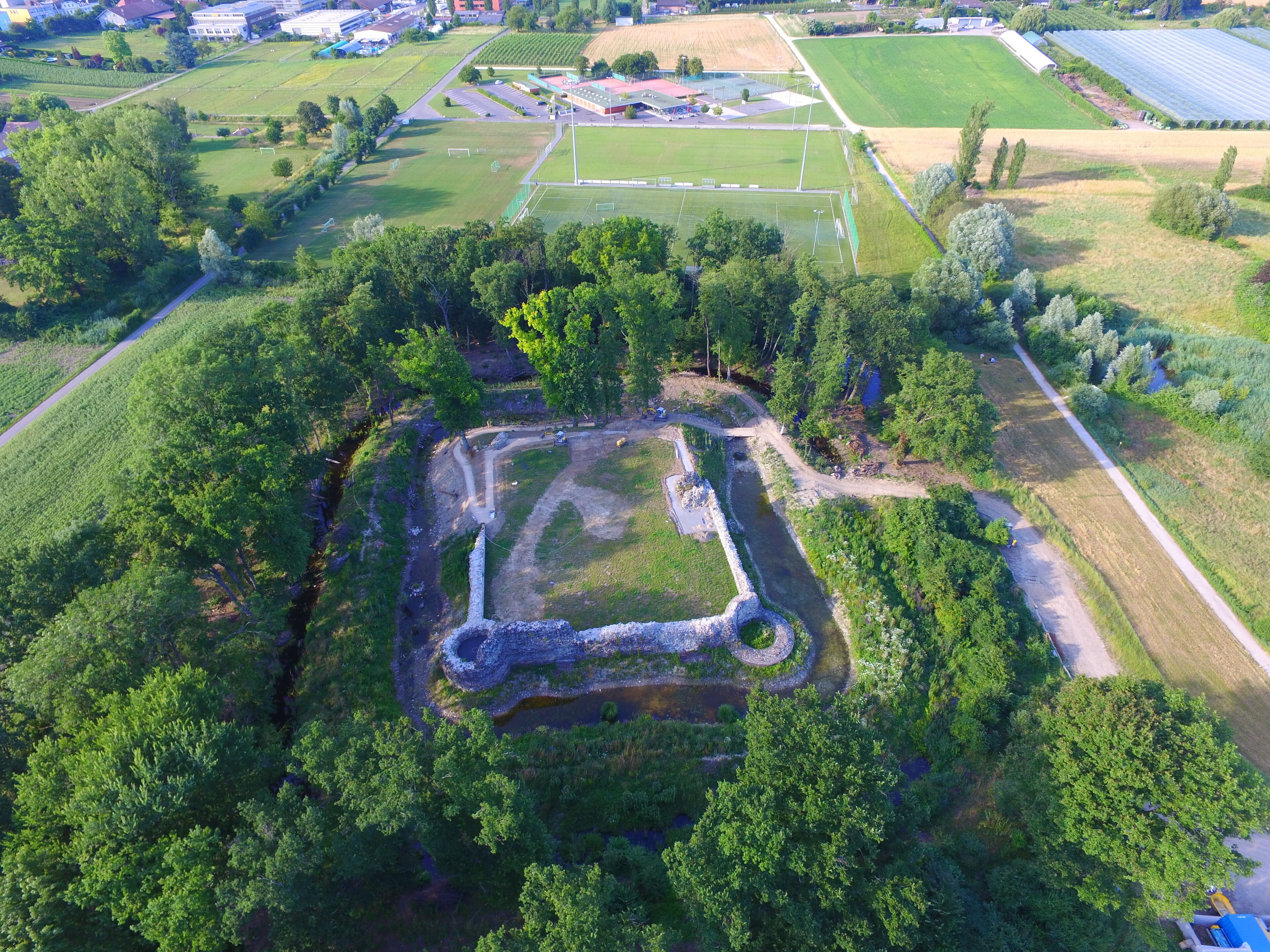 An aerial view of a park with a central square, surrounded by dense trees and fields.