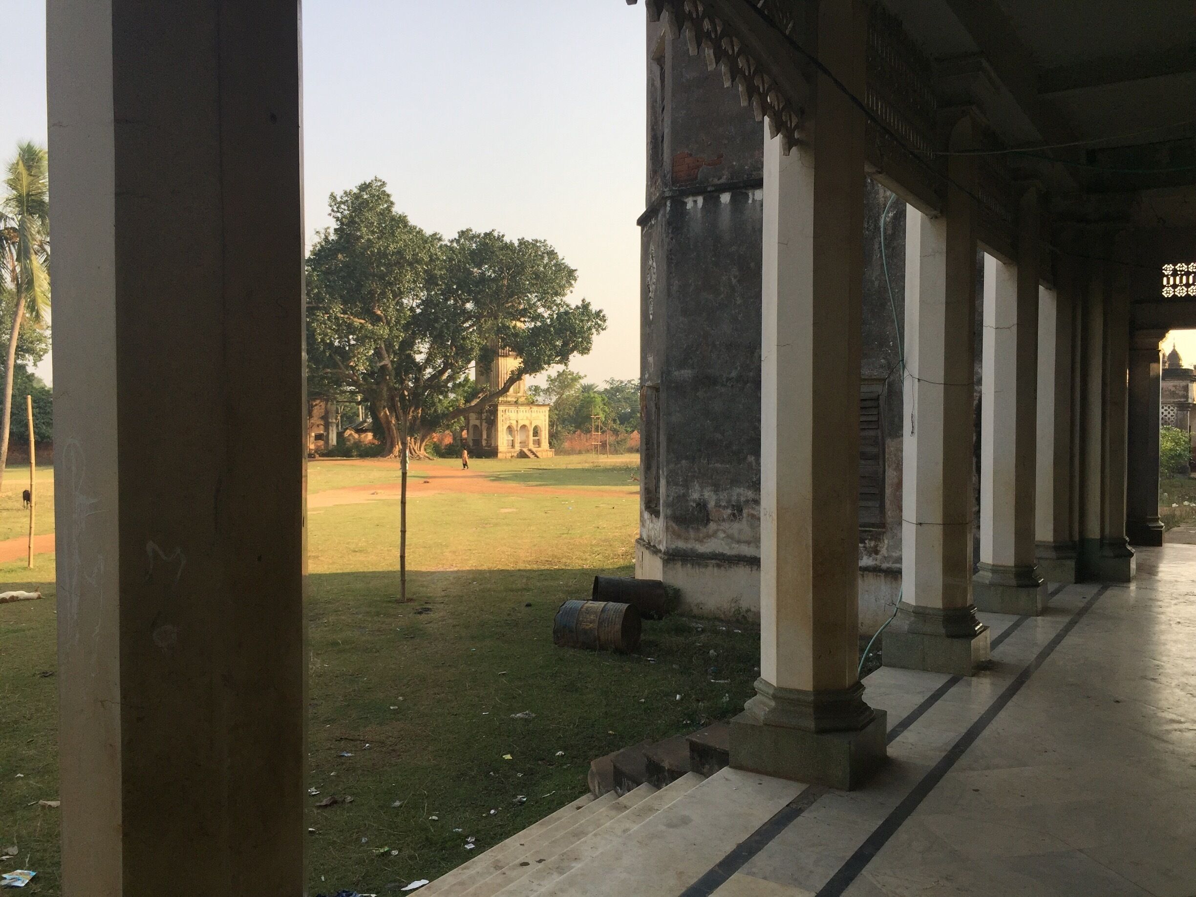 A covered walkway with columns, a grassy field, and a distant building.