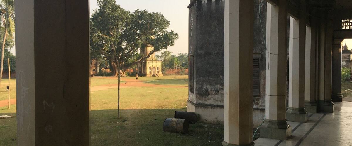 A covered walkway with columns, a grassy field, and a distant building.