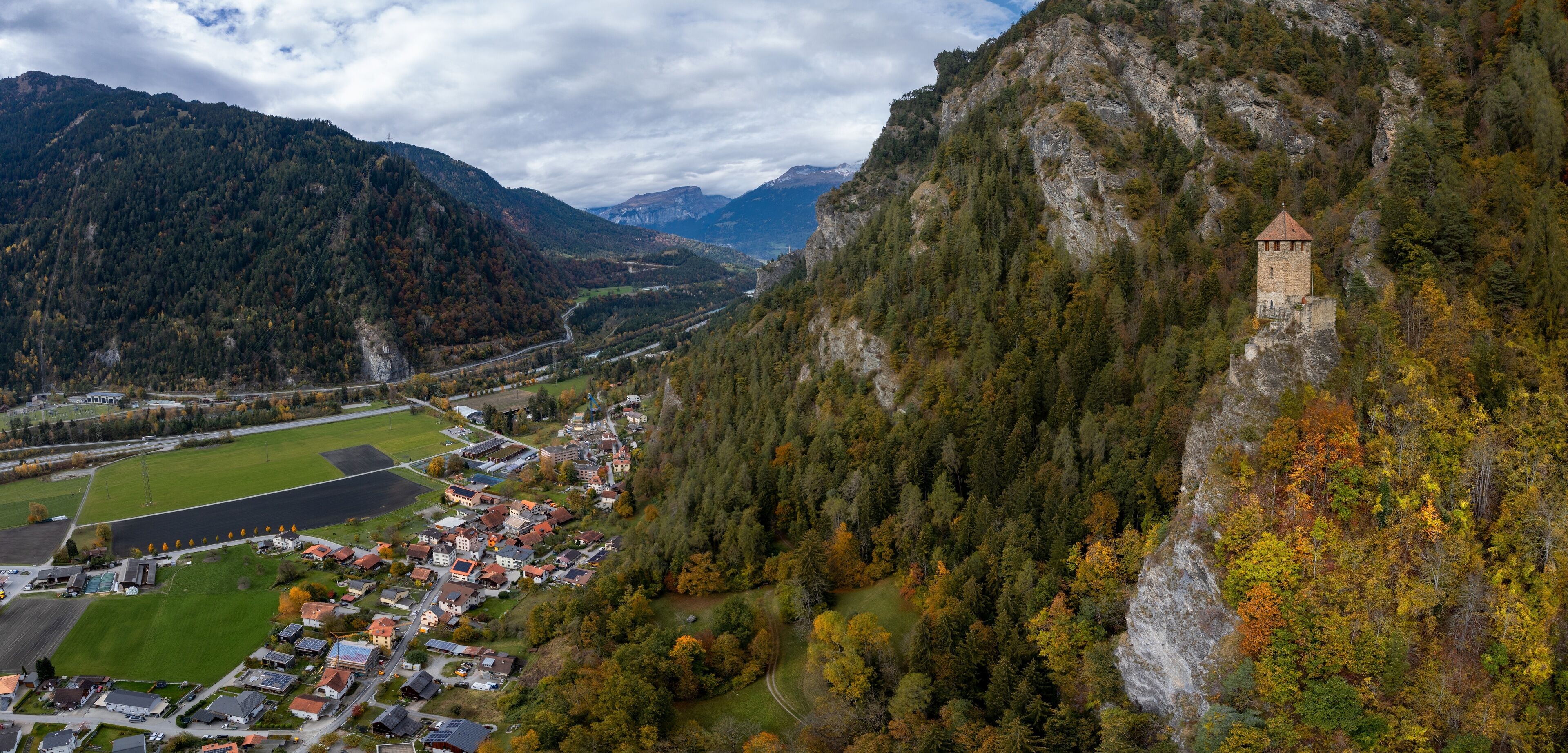 A mountainous landscape with a small town nestled in a valley, surrounded by dense forests and a prominent tower on a cliff.