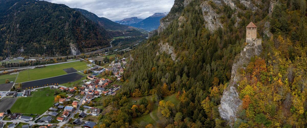 A mountainous landscape with a small town nestled in a valley, surrounded by dense forests and a prominent tower on a cliff.