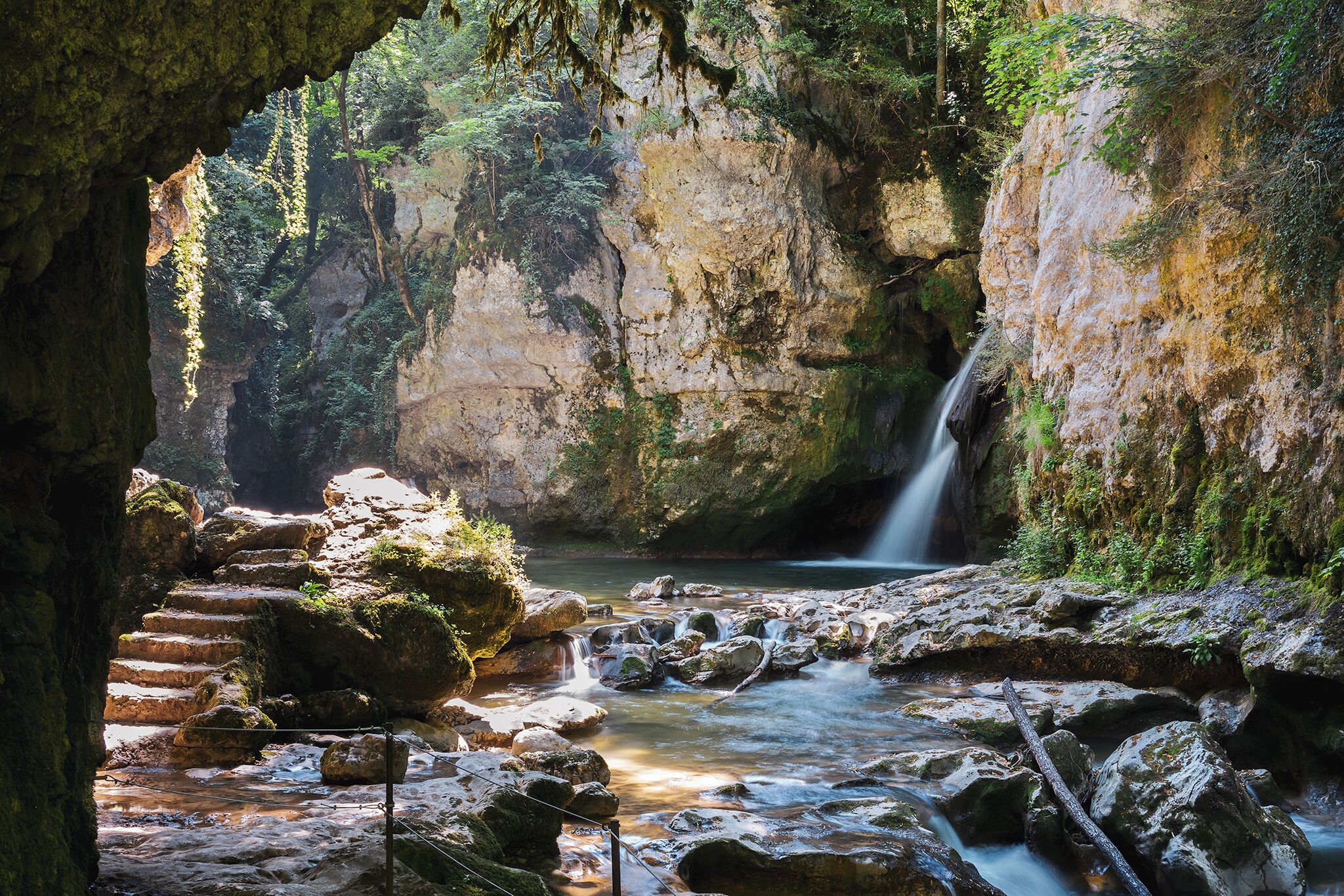 A natural cave entrance with a waterfall and a stream.