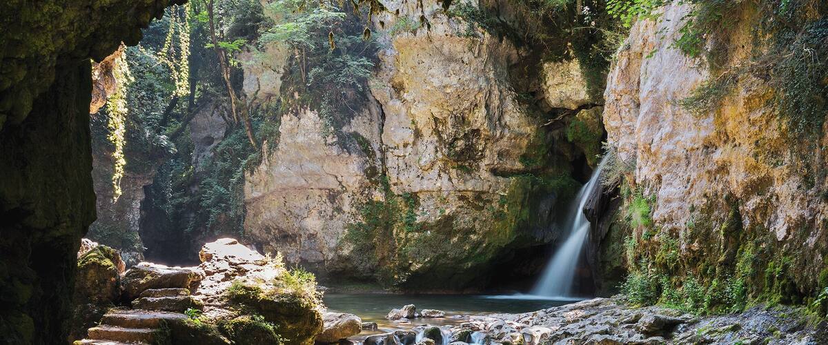 A natural cave entrance with a waterfall and a stream.