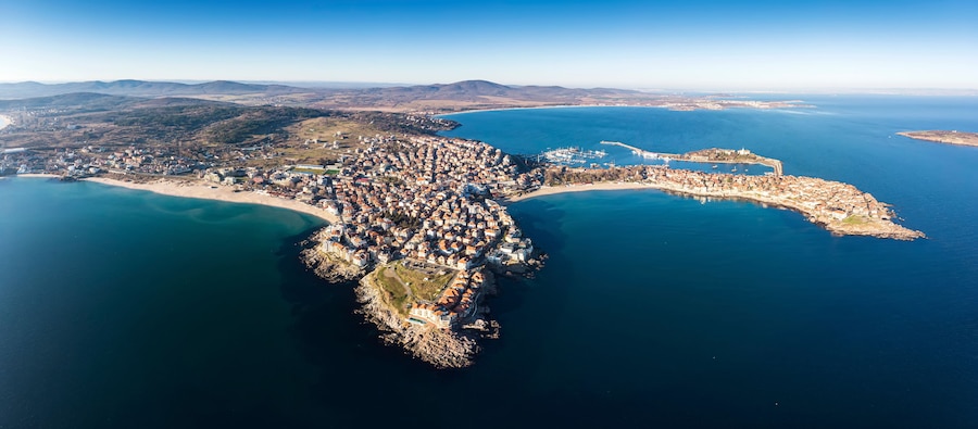 Vista aérea de un pueblo costero con una bahía, una playa y montañas al fondo.