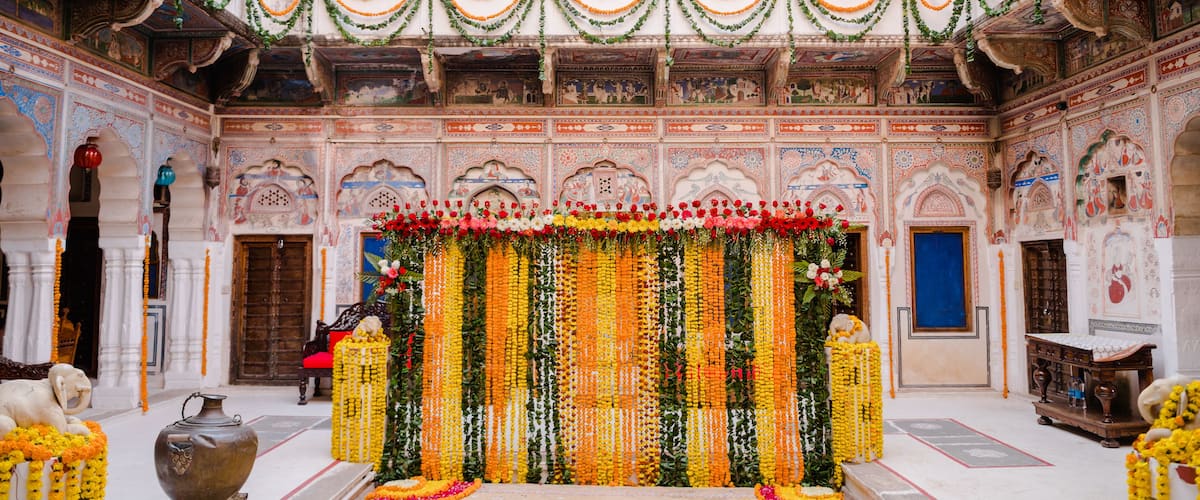 A decorated courtyard with intricate murals, a central floral arrangement, and traditional Indian artifacts.