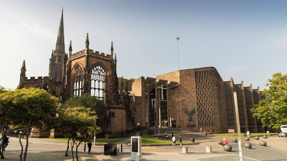 The Cathedral was built between 1956 and 1962 and was designed by Sir Basil Spence, following the destruction of the old mediaeval Cathedral in 1940 through enemy bombing. It was decided to build the new Cathedral adjacent to the old one, which was left in its semi-ruined state with its undamaged 14th century tower. It would in fact be the third Cathedral in Coventry, as this had been a religious site for nearly 1000 years. There was a competition for the design which was won by the Scottish architect Basil Spence. The unorthodox design was intended to be "a casket of jewels" and contains many works from famous artists. The Cathedral was consecrated on 25 May 1962. The Cathedral was built at right angles to the old one, and therefore aligns north-south. It is built in red Hollington sandstone with green slate cladding and a concrete roof. There is a nave of seven bays, although the aisles are full height, with slender piers tapering at the base. They rise to a concrete ribbed canopy with timber between the ribs. There is no clerestory. The nave walls are angled in a sawtooth fashion with tall stained-glass windows. The nave and chancel are as one. The (liturgical) west end has a fully glazed wall with engraved figures of saints and angels by John Hutton. The (liturgical) east wall has no window, but is dominated by a large tapestry of Christ in Glory by Graham Sutherland. There are two chapels, one to the north east (The Chapel of Christ the Servant) and one to the south west (The Chapel of Unity). The baptistery area to the south east has a full height slightly curved window with closely spaced mullions containing nearly 200 small windows. It was designed by John Piper and painted by Patrick Reyntiens. The font is made with a boulder from near Bethlehem. On the exterior wall is a sculpture by Epstein of Saint Michael and Lucifer. The low roof is crowned by a metal fleche topped by a cross. The organ is by Harrison and Harrison, divided in galleries either side of the altar. There is an open western (southern) porch linking the two cathedrals. There are also lower levels to the Cathedral with further display and administration rooms. There is also an attached cafe. Pic by Jenny
