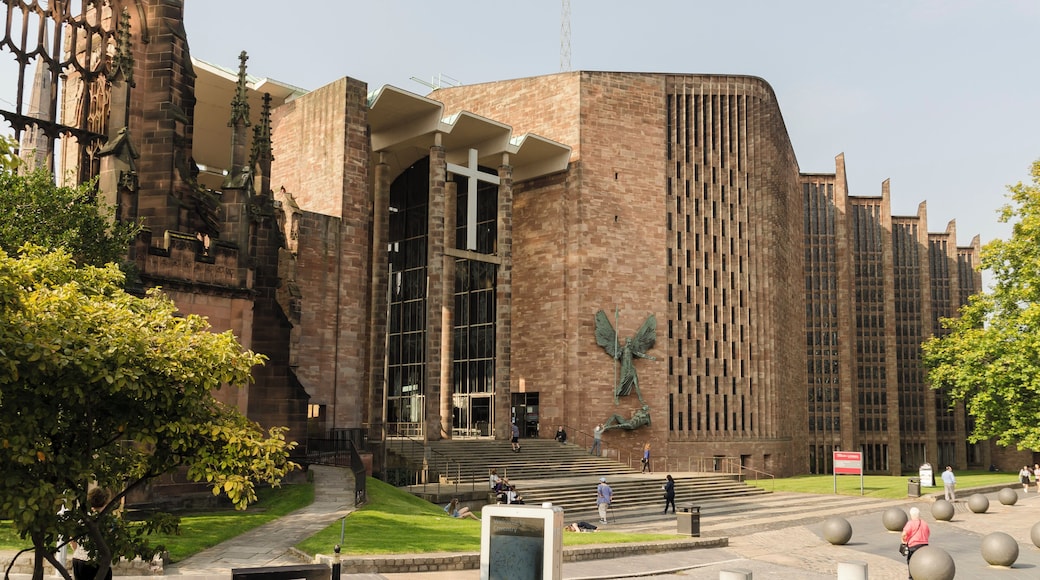 The Cathedral was built between 1956 and 1962 and was designed by Sir Basil Spence, following the destruction of the old mediaeval Cathedral in 1940 through enemy bombing. It was decided to build the new Cathedral adjacent to the old one, which was left in its semi-ruined state with its undamaged 14th century tower. It would in fact be the third Cathedral in Coventry, as this had been a religious site for nearly 1000 years. There was a competition for the design which was won by the Scottish architect Basil Spence. The unorthodox design was intended to be "a casket of jewels" and contains many works from famous artists. The Cathedral was consecrated on 25 May 1962. The Cathedral was built at right angles to the old one, and therefore aligns north-south. It is built in red Hollington sandstone with green slate cladding and a concrete roof. There is a nave of seven bays, although the aisles are full height, with slender piers tapering at the base. They rise to a concrete ribbed canopy with timber between the ribs. There is no clerestory. The nave walls are angled in a sawtooth fashion with tall stained-glass windows. The nave and chancel are as one. The (liturgical) west end has a fully glazed wall with engraved figures of saints and angels by John Hutton. The (liturgical) east wall has no window, but is dominated by a large tapestry of Christ in Glory by Graham Sutherland. There are two chapels, one to the north east (The Chapel of Christ the Servant) and one to the south west (The Chapel of Unity). The baptistery area to the south east has a full height slightly curved window with closely spaced mullions containing nearly 200 small windows. It was designed by John Piper and painted by Patrick Reyntiens. The font is made with a boulder from near Bethlehem. On the exterior wall is a sculpture by Epstein of Saint Michael and Lucifer. The low roof is crowned by a metal fleche topped by a cross. The organ is by Harrison and Harrison, divided in galleries either side of the altar. There is an open western (southern) porch linking the two cathedrals. There are also lower levels to the Cathedral with further display and administration rooms. There is also an attached cafe.