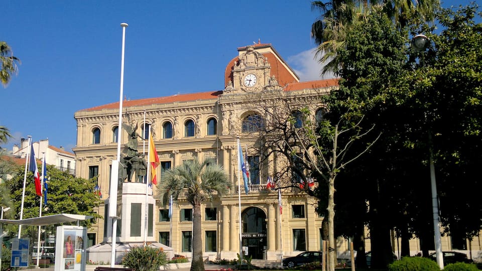 A historic building with a clock tower, ornate architecture, and multiple flags.