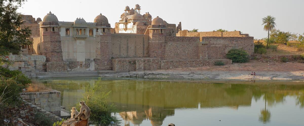 A historic fort with domed structures, a calm river, and monkeys sitting on rocks.