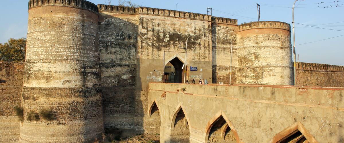 A historic stone bridge with arched stonework spanning a river, leading to a fortified structure with large cylindrical towers.