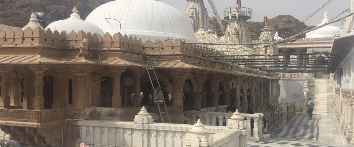 A temple with white domes and intricate carvings, a checkered pathway, and a mountainous backdrop.