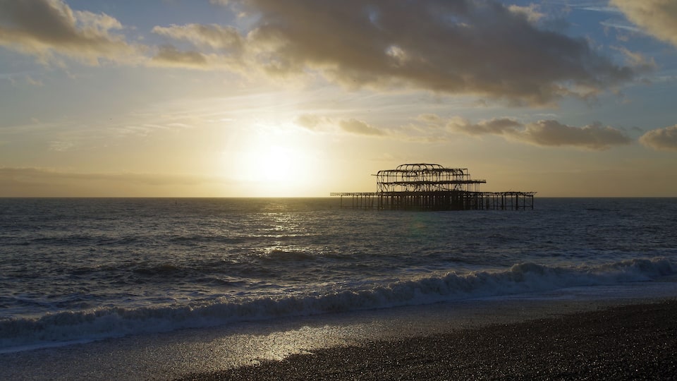 The remains of Brighton West Pier, seen from the beach as the sun sets.