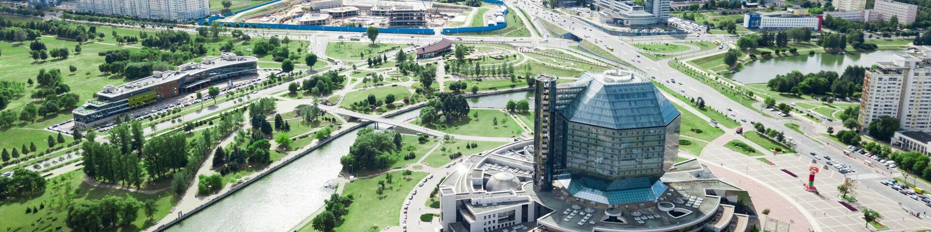 An aerial view of a city with a prominent circular building, a river, and surrounding greenery.
