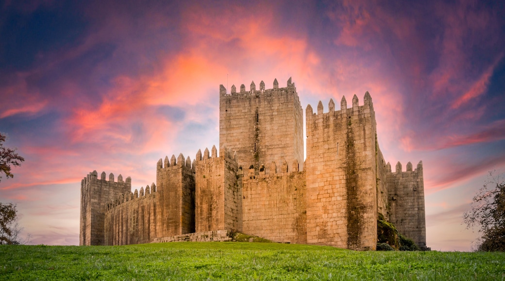 A historic castle with multiple towers and battlements, set against a dramatic sunset sky.