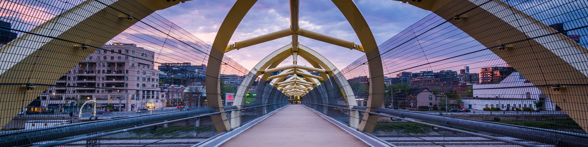 A pedestrian bridge with a geometric design, featuring a central walkway and railings on both sides.