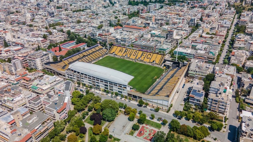 Thessaloniki, Greece landscape drone shot of ARIS FC Charilaou stadium. Aerial top day view of empty football court Kleanthis Vikelidis with green pitch & team name written on stands.