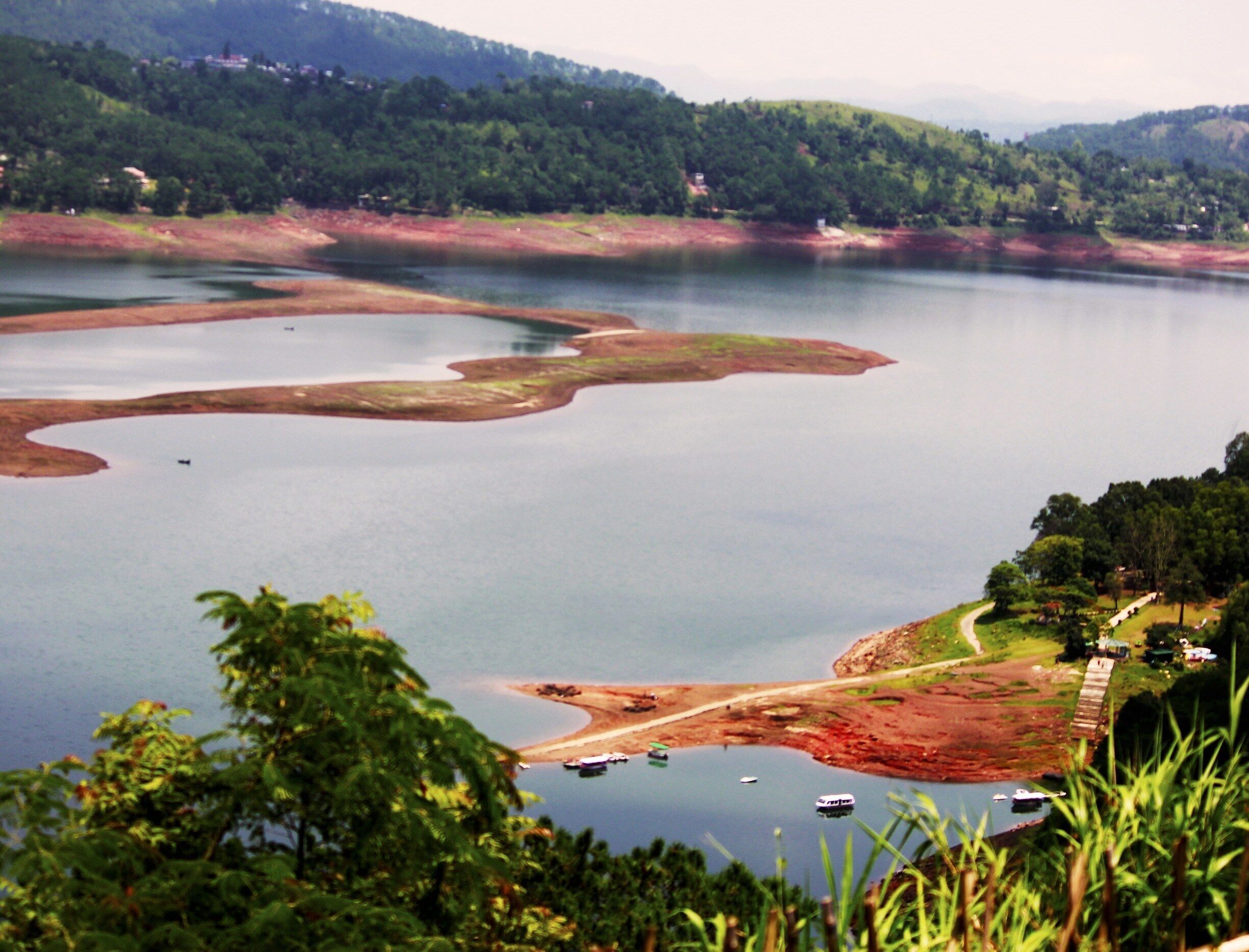 A lake surrounded by hills and trees. Boats are visible on the water.