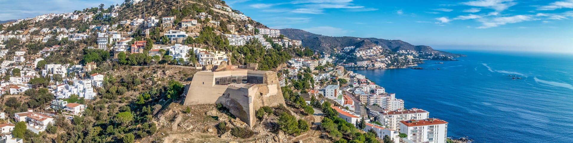 A coastal town with terraced fields, a prominent hilltop structure, and a clear view of the sea.