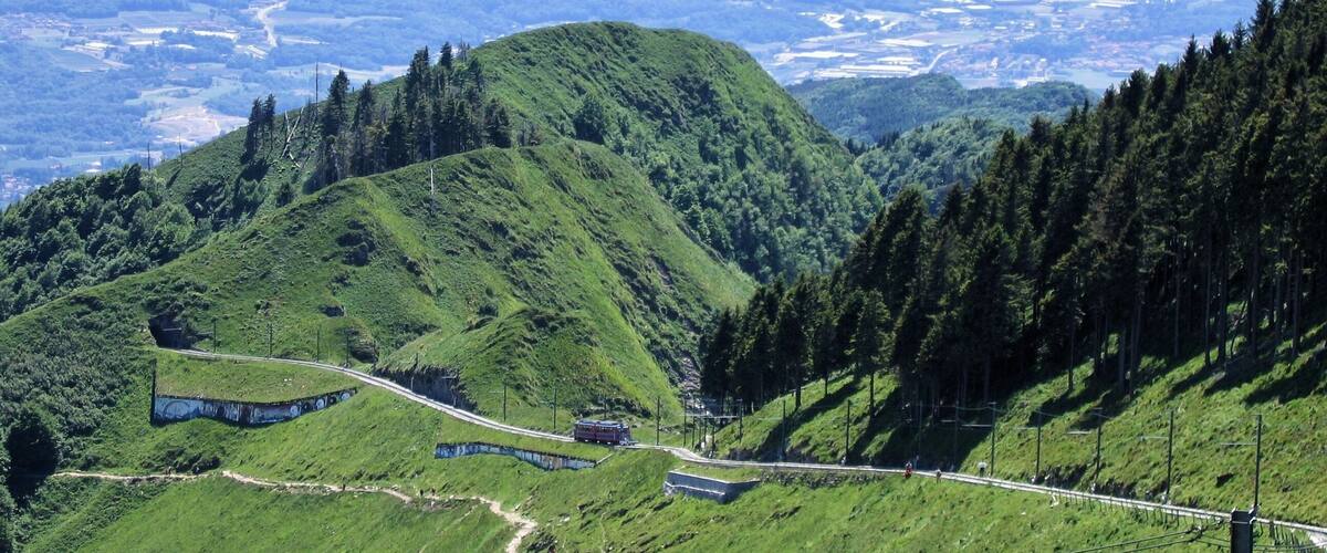 A mountainous landscape with a winding road, a red bus, and dense forest.