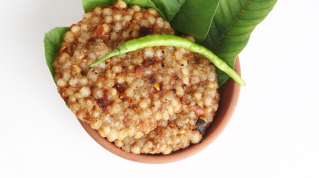A crisp fried India snack called Sabudana Vada made from tapioca seeds, roasted peanuts, boiled potato and herbs served in a terracotta bowl placed on a white background