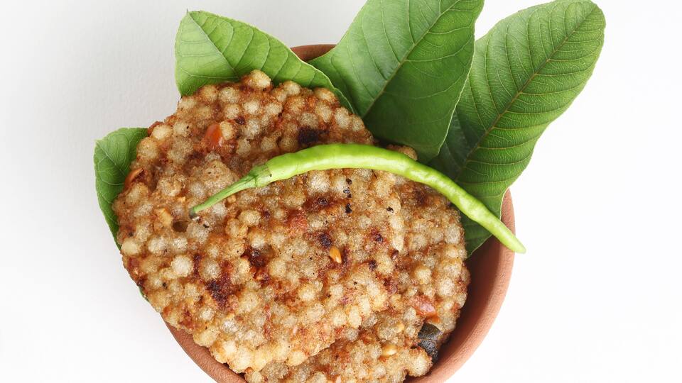 A dish with a green chili and leaves on a clay plate.