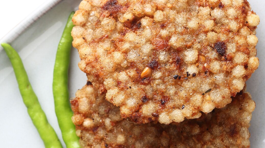 A crisp fried India snack called Sabudana Vada made from tapioca seeds, roasted peanuts, boiled potato and herbs served in white plate placed on a white background