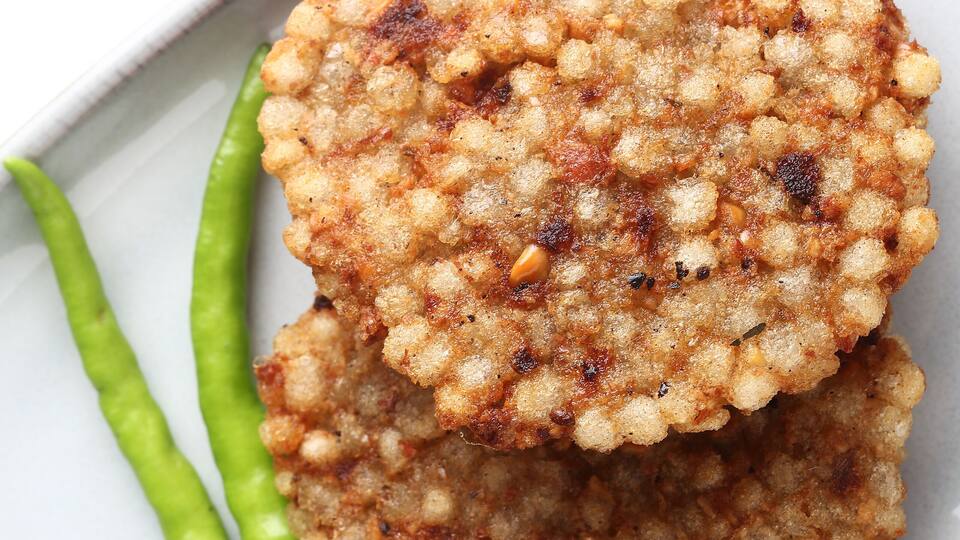Two fried patties with green chilies on a white plate.