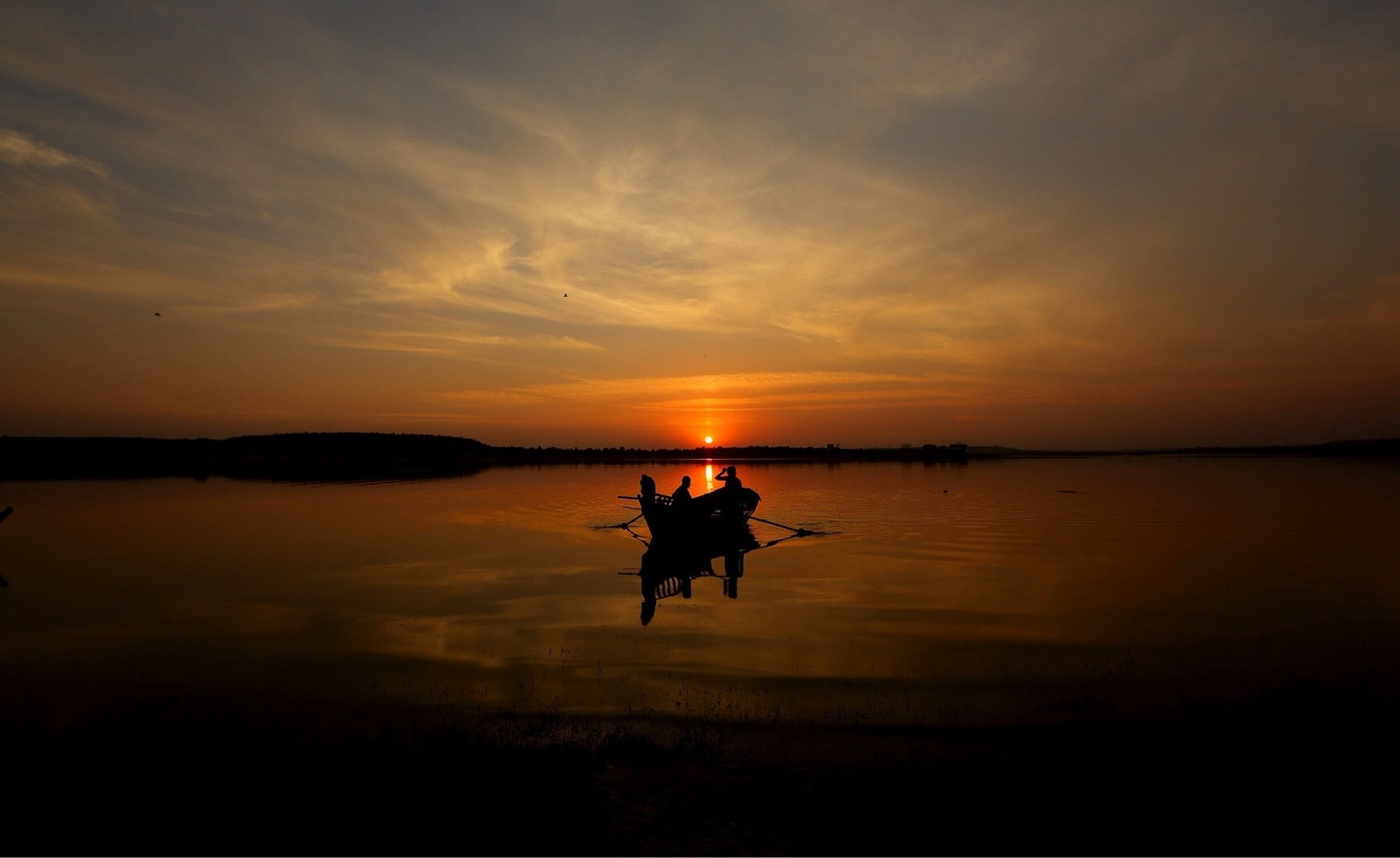 A sunset over a calm lake with a silhouette of a boat and people.