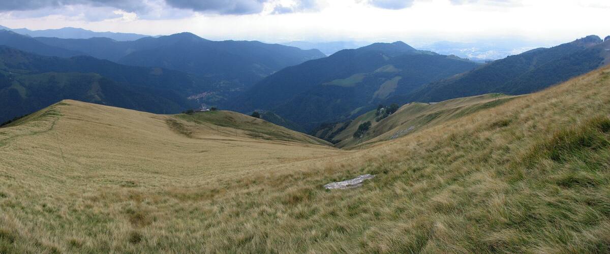 A grassy valley with rolling hills and distant mountain ranges under a cloudy sky.