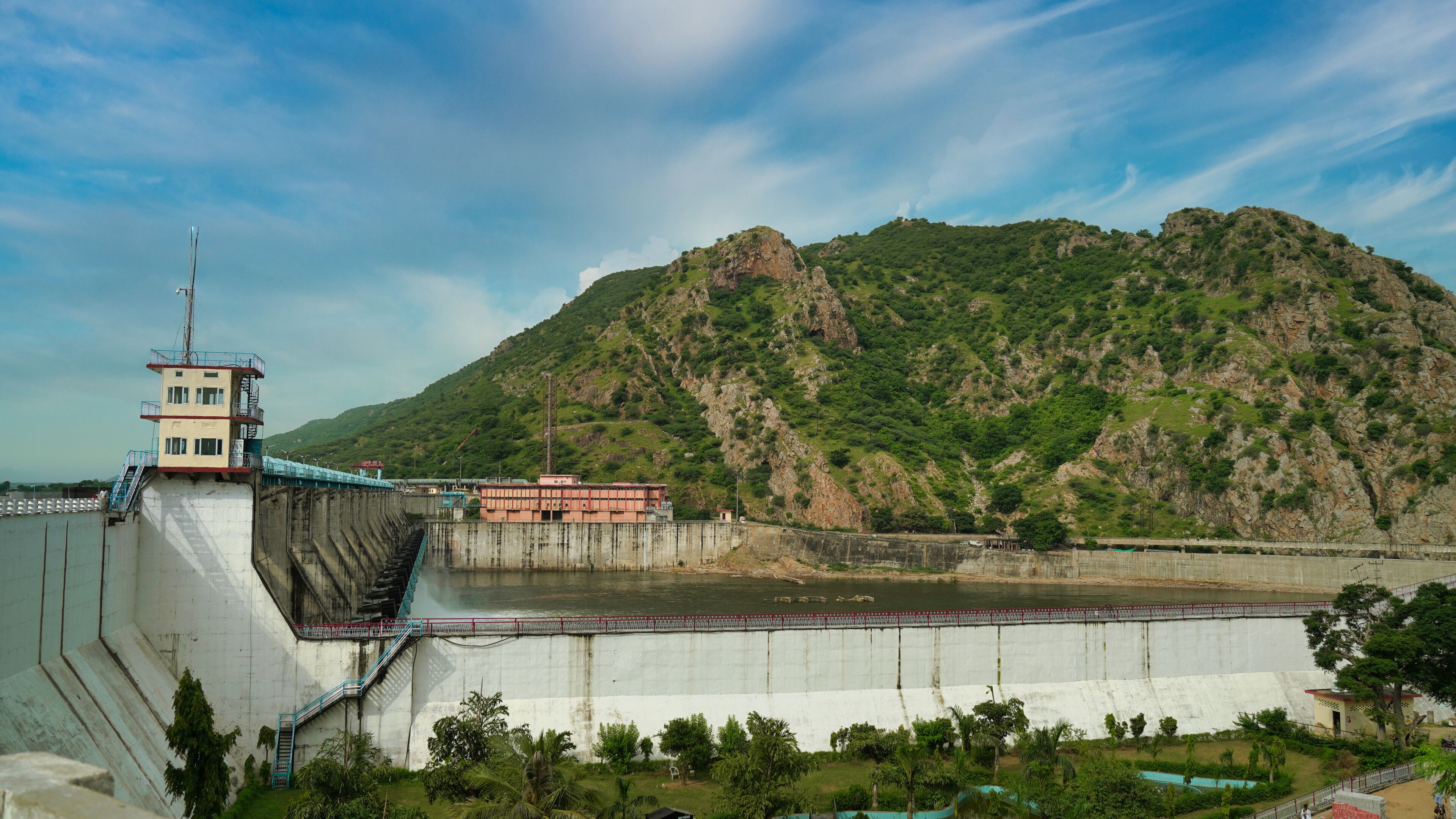 A dam with a control tower and a bridge across a river, surrounded by green hills.