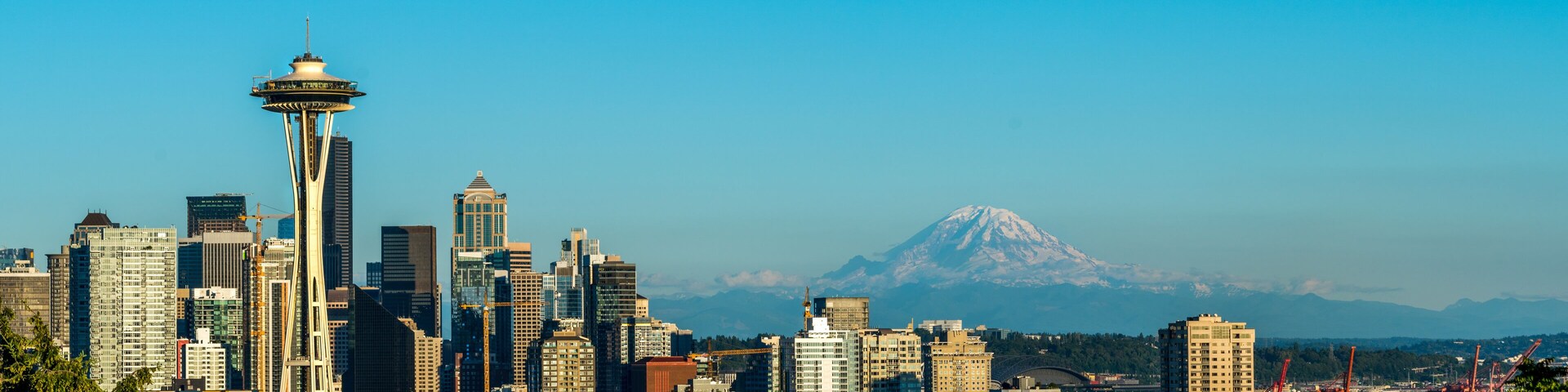 Wide panorama of sunset above Space Needle, with Mount Reinier in the background.