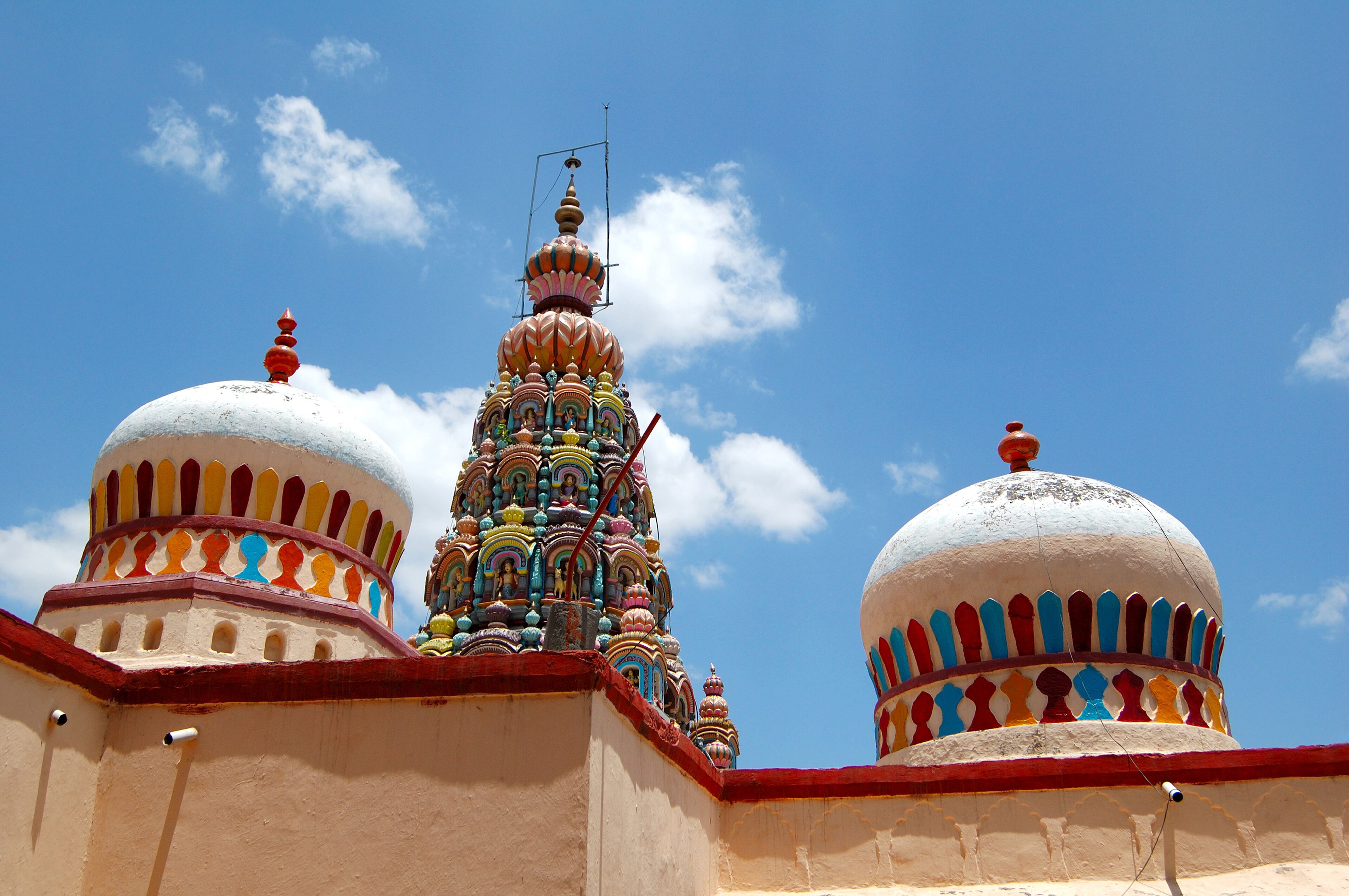 A colorful temple with multiple domes and intricate designs against a clear blue sky.