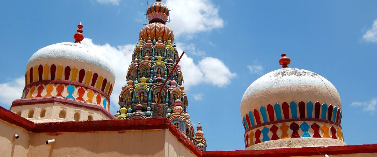 A colorful temple with multiple domes and intricate designs against a clear blue sky.