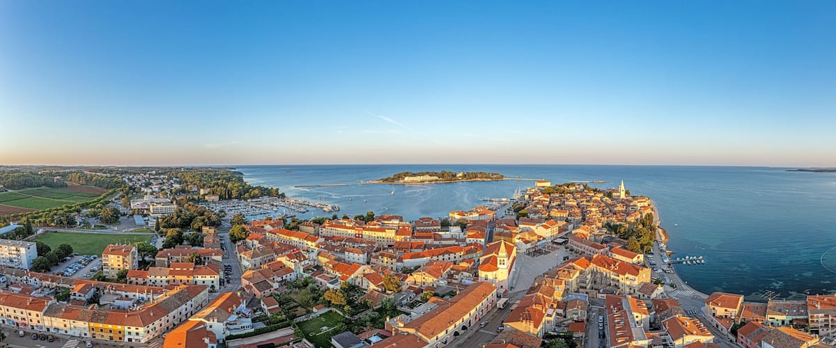 A coastal town with red-roofed buildings, a marina, and a distant island.