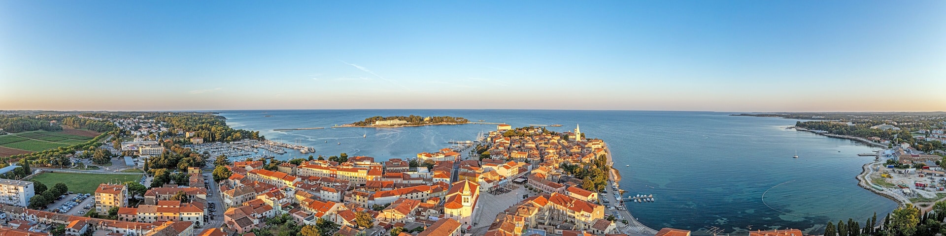 A coastal town with red-roofed buildings, a marina, and a distant island.