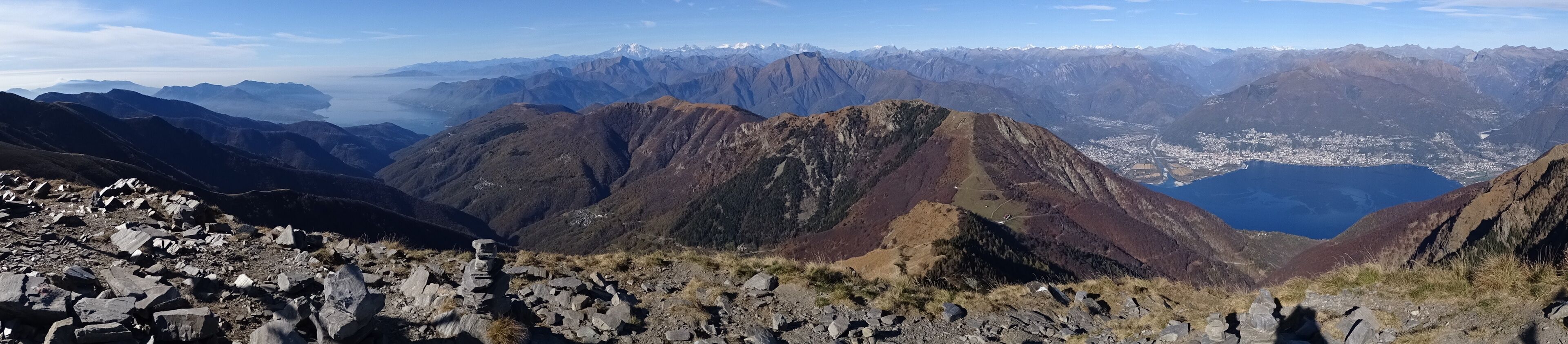 A mountainous landscape with rocky terrain and a valley with a lake and a town in the distance.