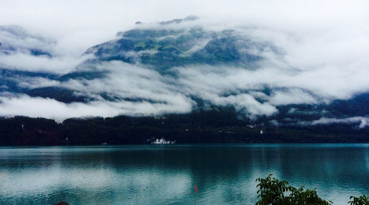 A mountain partially obscured by clouds, a calm lake, and a small island with a structure.