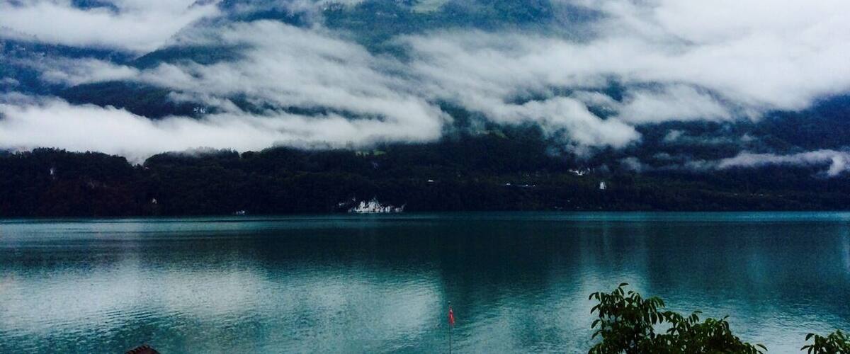 A mountain partially obscured by clouds, a calm lake, and a small island with a structure.