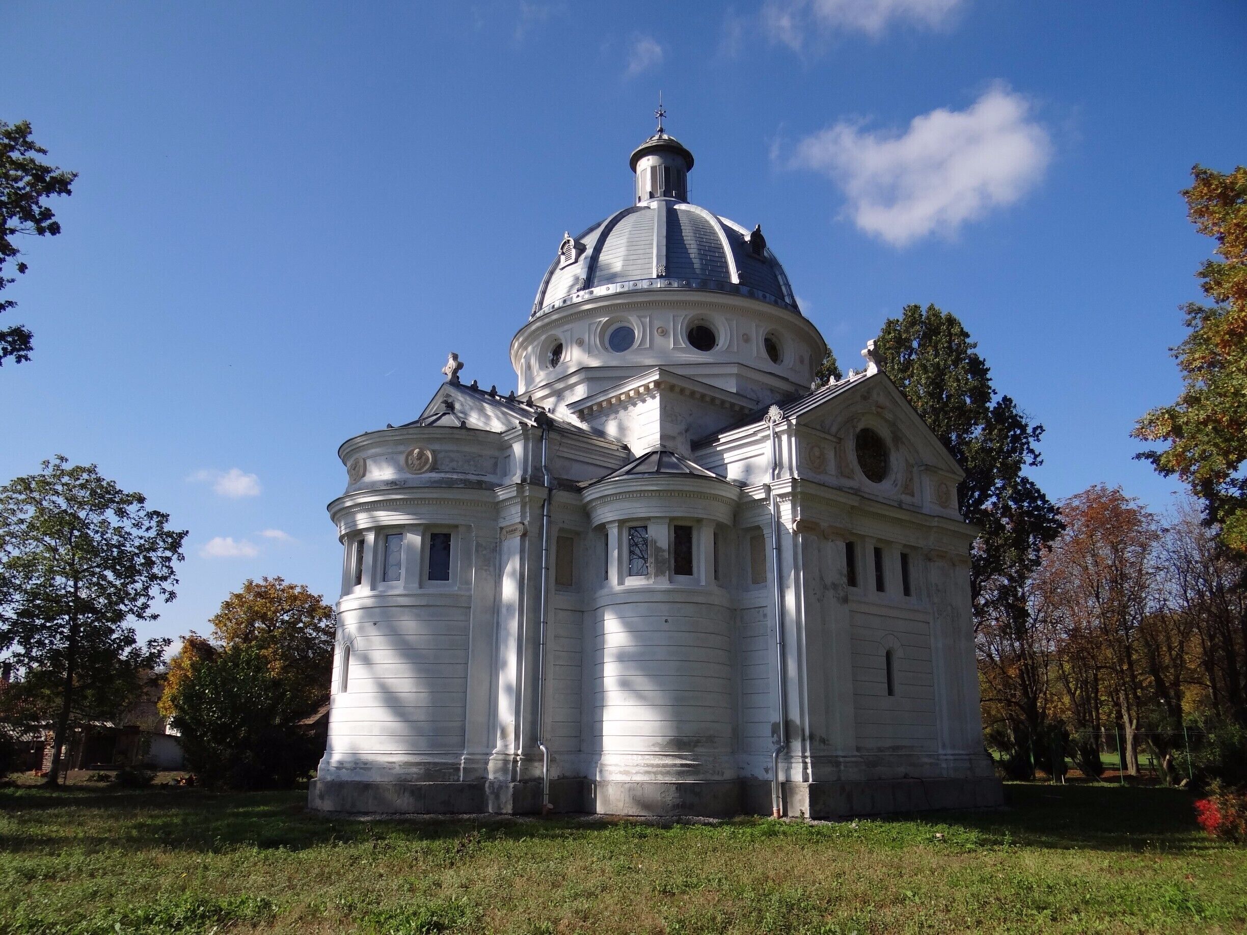 A classical white building with a large dome and multiple smaller domes, surrounded by trees and grass.