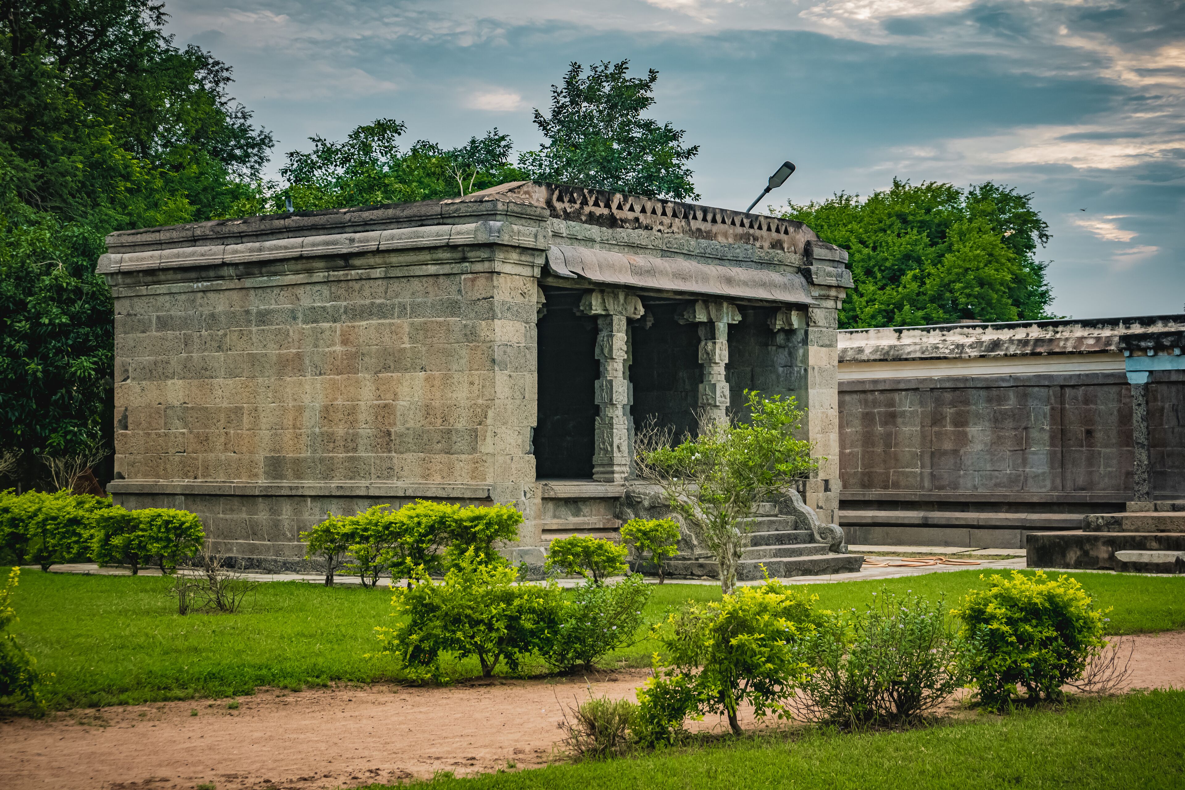A stone structure with columns, surrounded by greenery and trees.
