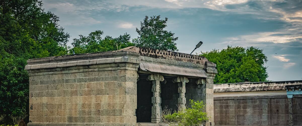 A stone structure with columns, surrounded by greenery and trees.