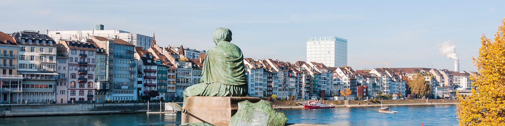 A statue of a seated figure overlooking a river with buildings in the background.