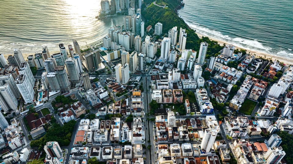 Un paisaje urbano costero con rascacielos, una playa y una zona montañosa con abundante vegetación.